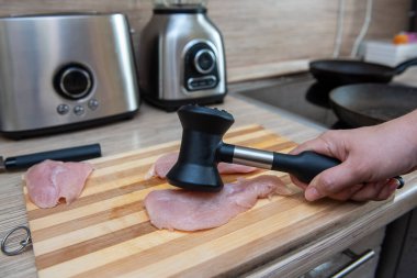 Kadın elleri tavuk filetosunu çekiçle döver..