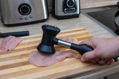 Kadın elleri tavuk filetosunu çekiçle döver..