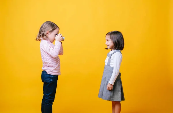 Sarı arka planda fotoğraf makinesi olan iki kız.