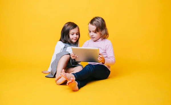 İki kız sarı arka planda dijital tablet kullanıyor.