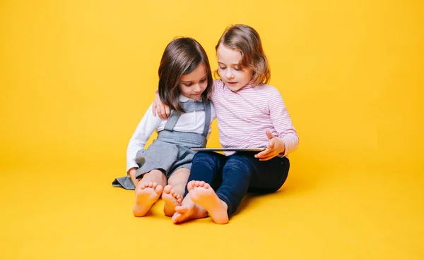 Dos chicas usan una tableta digital sobre un fondo amarillo —  Fotos de Stock