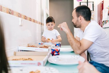 Bir aile kendi mutfağında pizza yer.