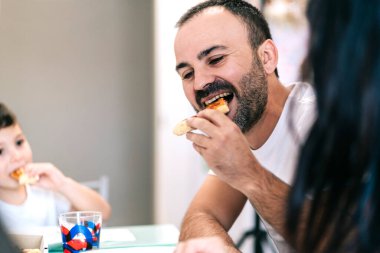Bir aile kendi mutfağında pizza yer.