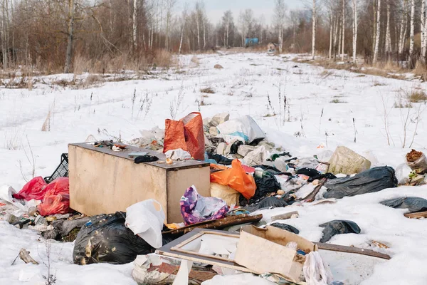 Bags of garbage in the snow in the dacha village on the background of a glade