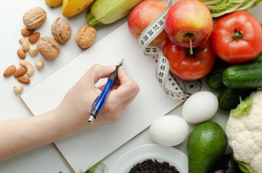 Kız diyet yapmayı planlıyor ve bir deftere yazıyor. Sağlıklı beslenme.