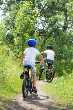 Parlak elbiseli iki kardeş ormanda bisiklet sürüyor..