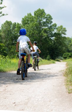 Parlak elbiseli iki kardeş orman yolunda bisiklet sürüyor..
