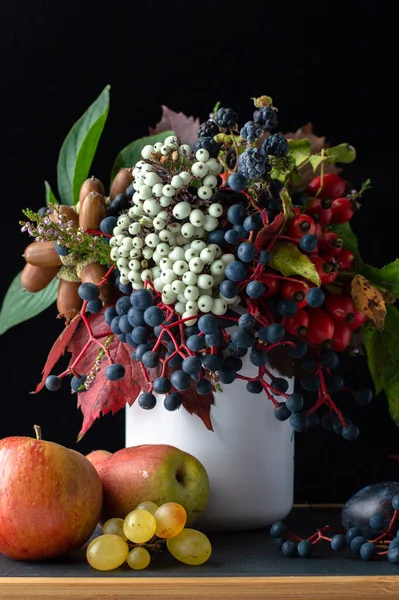 Autumn still life with fruits and a bouquet of berries and leaves on a dark background.