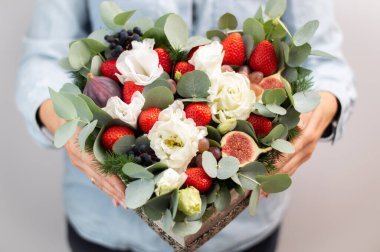 Kız elinde parlak bir buket çiçek ve böğürtlen tutuyor kalp şeklinde bir kutuda..