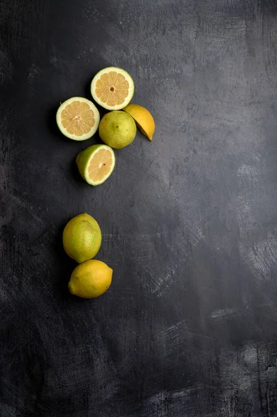 a set of yellow and green lemons, cut and uncut, on a background of dark, black, cement, metallic, marble and stone