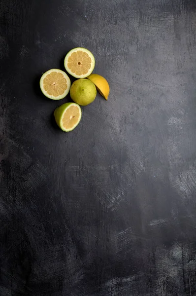 a set of yellow and green lemons, cut and uncut, on a background of dark, black, cement, metallic, marble and stone