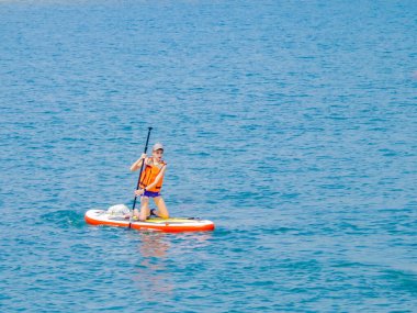 Sörf tahtasında sörf yapan genç bir sürücü, aktif yaşam tarzı kavramı olan kürekle bir dalgayı tırmıklıyor..