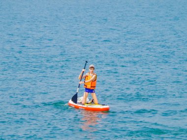 Sörf tahtasında sörf yapan genç bir sürücü, aktif yaşam tarzı kavramı olan kürekle bir dalgayı tırmıklıyor..