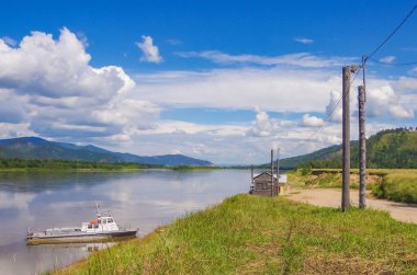 Nehrin kırsal kesiminde yaz manzarası. Ormanın ortasında sessiz bir nehir ve kıyıya demirlemiş eski bir tekne.