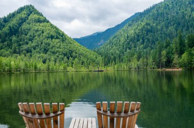 Plajda iki boş tahta sandalye, dağ gölünün güzel manzarası, dağlarda tatil, lüks yaz tatili konsepti.