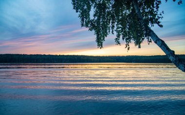 Sakin bir nehrin üzerinde yaz günbatımı manzarası.