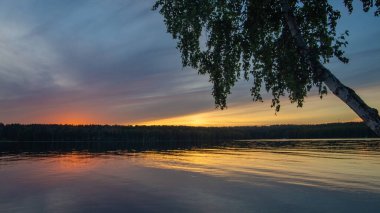 Sakin bir nehrin üzerinde yaz günbatımı manzarası.