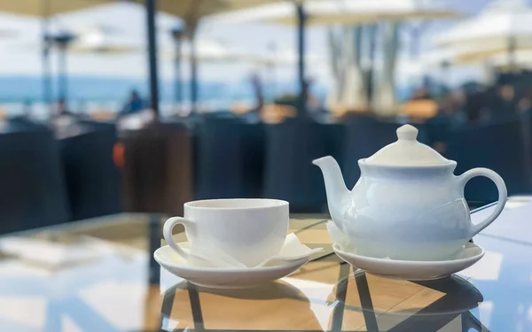 Çay demleyicisi için çaydanlık ve açık kafedeki masada beyaz bardak.