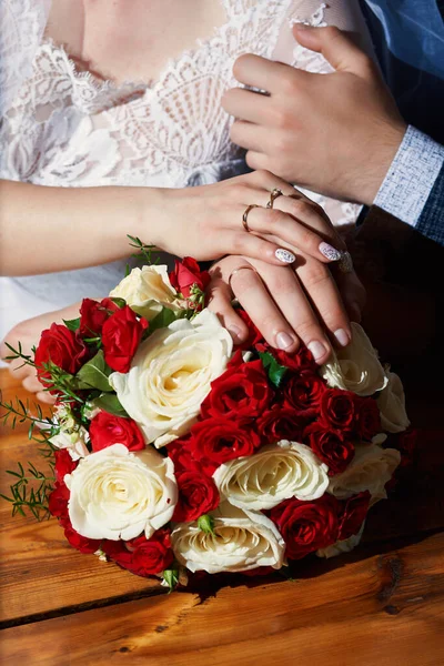 Gelin ve damadın düğün buketinde nazikçe el ele tutuşurken çekilmiş dikey fotoğrafı.