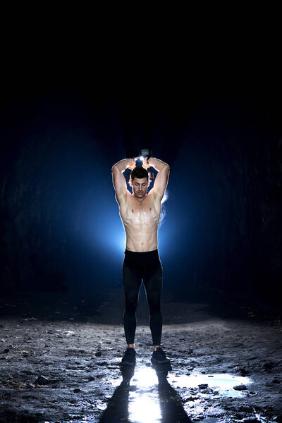 Сильный молодой мужчина поднимает гантели в пещере
