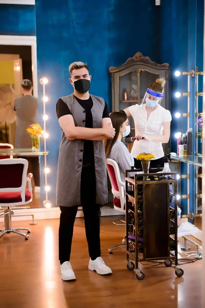 Yüzlerinde maskeler olan profesyonel kuaförler COVID-19 salgını sırasında güzellik salonunda bir kadının saçını yapıyor..