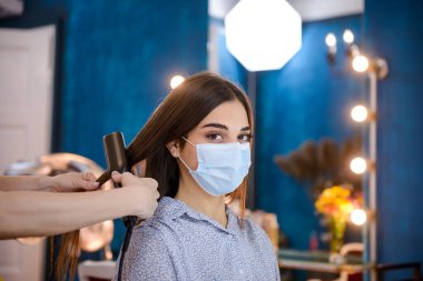 Yüzlerinde maskeler olan profesyonel kuaförler COVID-19 salgını sırasında güzellik salonunda bir kadının saçını yapıyor..