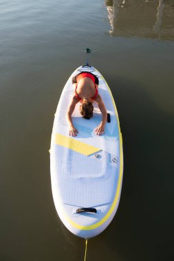 Güneş doğarken kürek tahtasında yoga yapmaya hazırlanan bir kadın.