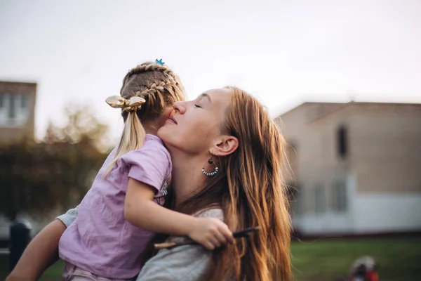 Mujer feliz sosteniendo a su hija pequeña, al aire libre al atardecer, hermosa mujer abraza a su hija pequeña, cara sonriente, retrato — Foto de Stock