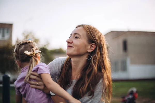 Mujer feliz sosteniendo a su hija pequeña, al aire libre al atardecer, hermosa mujer abraza a su hija pequeña, cara sonriente, retrato — Foto de Stock