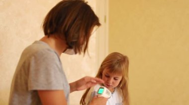 Anne, kızının sıcaklığını evinde elektronik termometreyle ölçüyor..
