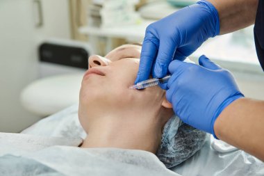 Güzellik salonundaki eldiven uzmanı hastanın yüzüne şırınga enjekte ediyor..