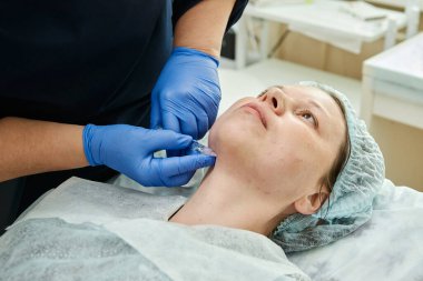 Eldiven uzmanı, kanepede yatan genç bir kadının çenesine şırınga enjekte ediyor..