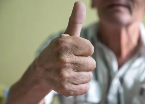 Close-up Pensioner shows thumbs up. A positive elderly man held out his hand and showed a thumbs up. Selective focus, shallow depth of field