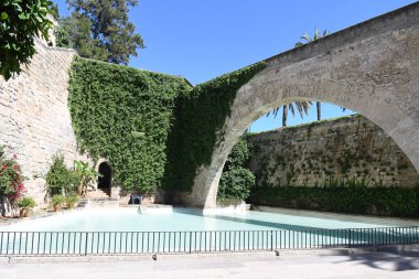 Sarmaşık duvarlı ve kemerli kaledeki yapay gölet manzarası