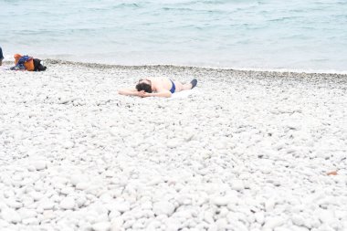 Çakıl taşlı plajda dinlenen insanlara bakın.