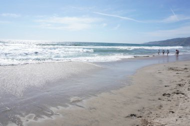 Okyanus kıyısı manzarası, kumdaki ayak izleri ve uzaktaki insanlar. 