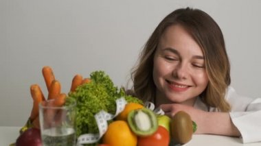 Diyet ve sağlık. Kafkas görünümlü bir kadın doktor masayı yalıyor ve meyve ve sebzelere hayran kalıyor.