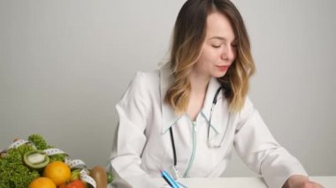 Bir beslenme uzmanı masasına sağlık hapları için reçete yazar. Sebzeler ve meyveler masada.