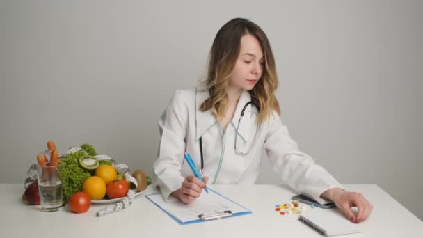 Een voedingsdeskundige schrijft een recept voor gezondheidspillen op zijn bureau. Groenten en fruit op tafel — Stockvideo