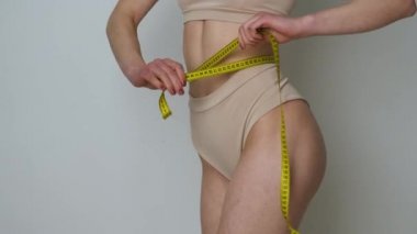 Kahverengi iç çamaşırlı ince bir kızın portresi. Diyet üstüne mezura ile belini ölçen ya da egzersiz yapan.