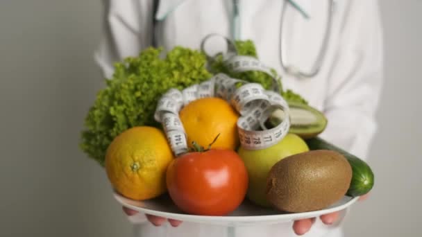 Nutricionista femenina en un abrigo blanco sosteniendo un plato con verduras y foros sonriendo a la cámara — Vídeo de stock