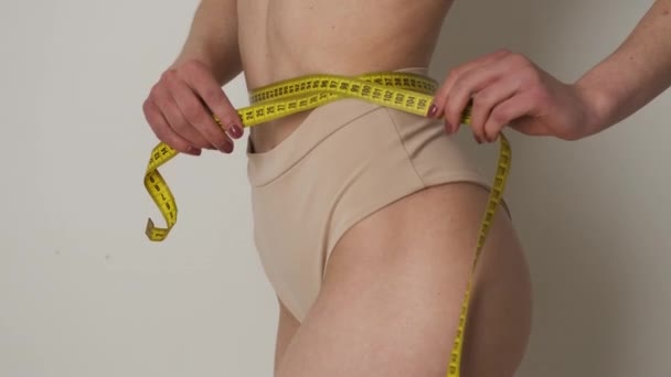 Retrato de uma menina delgada em lingerie marrom que mede a cintura com uma fita métrica após a dieta ou exercício — Vídeo de Stock