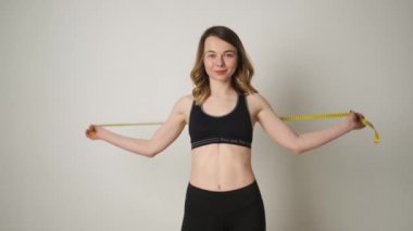 Spor giyimli ince bir kızın portresi. Vücut ölçülerini egzersiz üstüne mezurayla ölçen ve sonuçtan memnun olan.