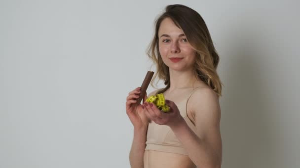 Slender athletic woman in brown lingerie holds a measuring tape in her hands and refuses high-calorie waffles — Stock Video