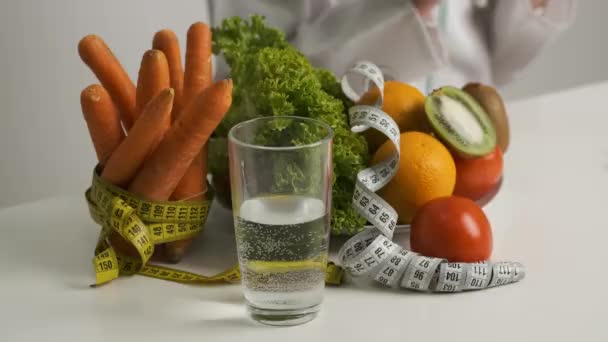 Zöldségek és gyümölcsök az asztalon az egészséges étrendért. Fogyókúra. Saláta, sárgarépa, egy pohár víz, kivi, paradicsom, narancs és mérőszalag — Stock videók