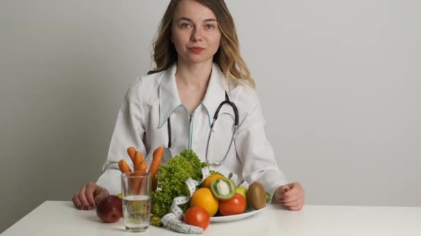 Dieta y salud. Una doctora de apariencia caucásica se sienta en una mesa y mira verduras y frutas — Vídeos de Stock