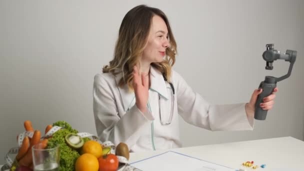 Um médico-nutricionista em sua mesa realiza treinamento on-line para seus clientes por videochamada pelo telefone — Vídeo de Stock