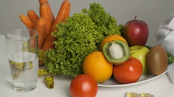 Grönsaker och frukt på bordet för en hälsosam kost. Föda. sallat, morötter, ett glas vatten, kiwi, tomat, apelsin och måttband — Stockvideo