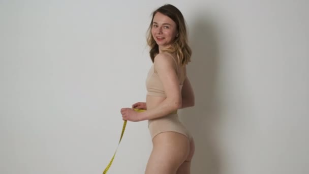 Karcsú lány barna fehérneműben, aki méri a derekát egy mérőszalaggal diéta után, és elégedett az eredmény az ő szám — Stock videók