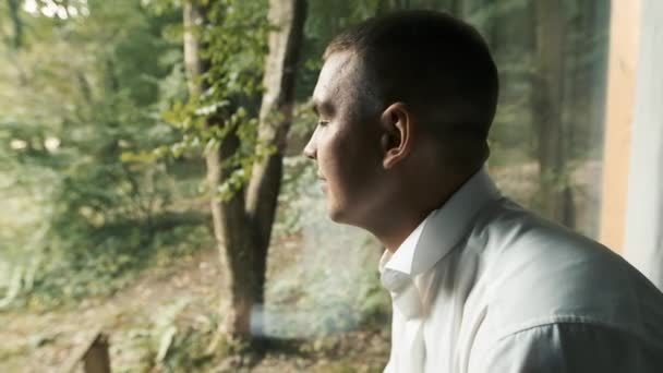 Mladý muž bělošského vzhledu s hnědýma očima sedící u panoramatického okna a přemýšlející o obchodním plánu — Stock video
